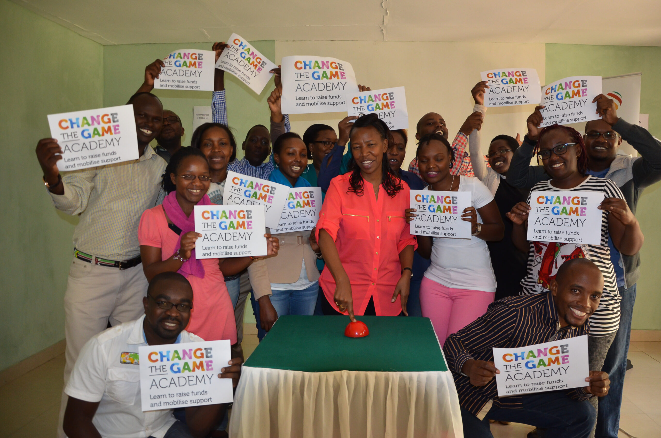 Een groep mensen die papieren in de lucht houden met logo van Change the Game Academy.
